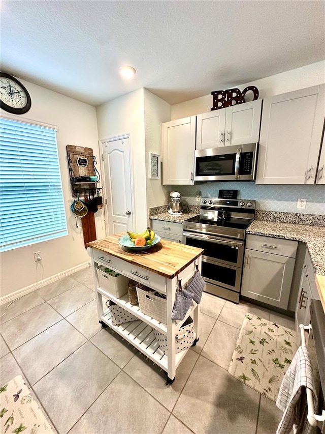 kitchen with baseboards, a textured ceiling, appliances with stainless steel finishes, and light tile patterned flooring