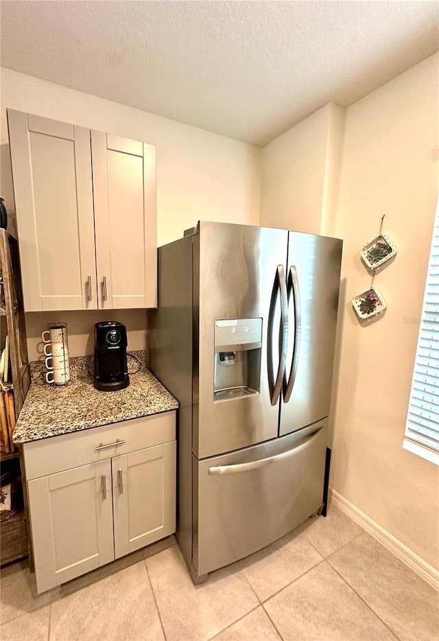 kitchen with light tile patterned floors, light stone countertops, baseboards, stainless steel fridge with ice dispenser, and a textured ceiling