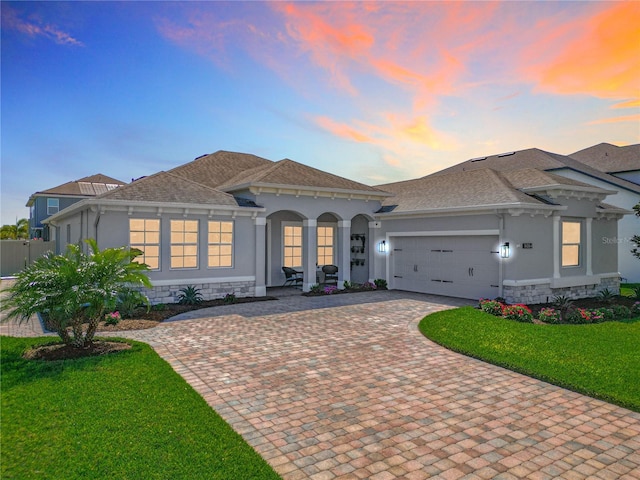 mediterranean / spanish-style home featuring an attached garage, stucco siding, stone siding, decorative driveway, and a lawn