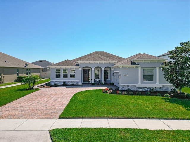 mediterranean / spanish home featuring stone siding, stucco siding, decorative driveway, and a front yard