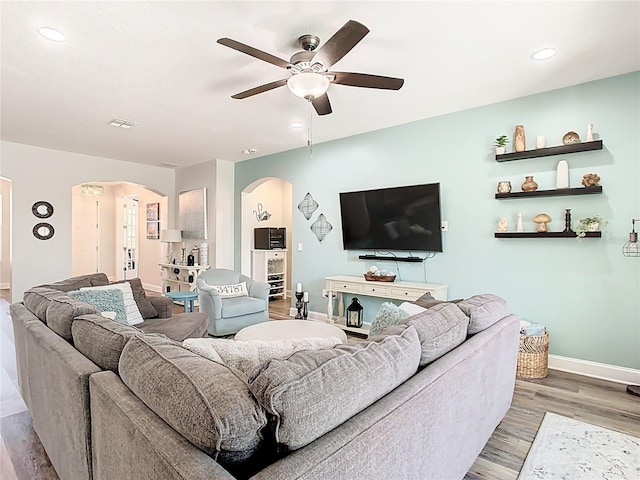 living room with visible vents, baseboards, wood finished floors, arched walkways, and a ceiling fan