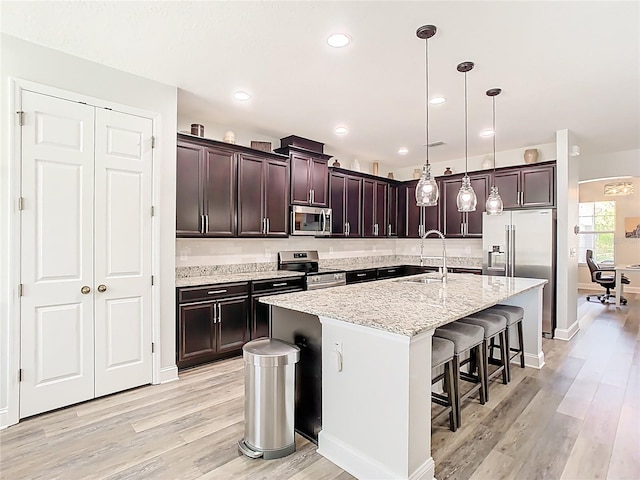 kitchen with dark brown cabinets, light stone counters, appliances with stainless steel finishes, light wood-style floors, and a sink