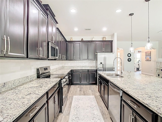 kitchen featuring tasteful backsplash, light stone countertops, decorative light fixtures, stainless steel appliances, and a sink