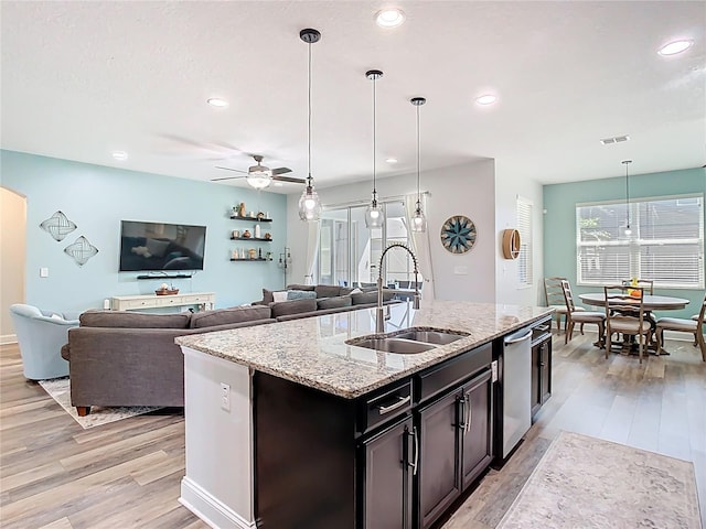 kitchen with light stone counters, light wood-style flooring, a sink, hanging light fixtures, and stainless steel dishwasher