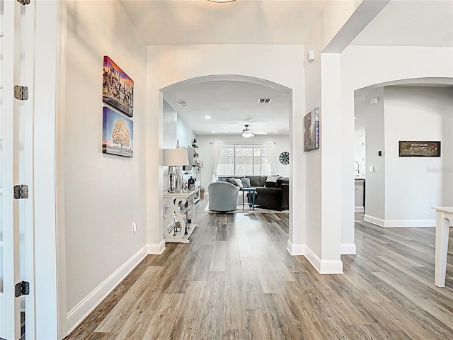 hall featuring arched walkways, baseboards, and wood finished floors