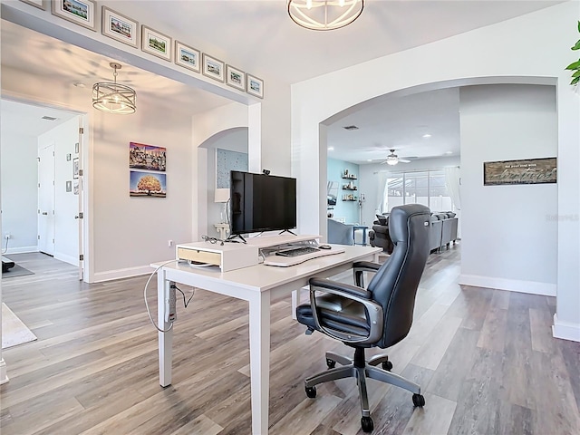 office space with arched walkways, a ceiling fan, baseboards, and wood finished floors