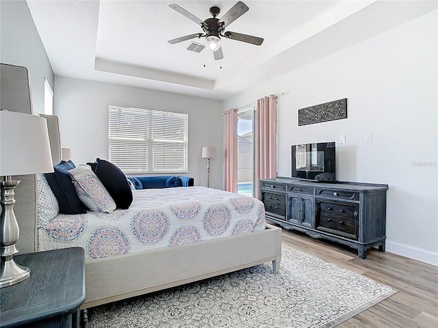 bedroom featuring ceiling fan, baseboards, light wood-style flooring, a raised ceiling, and access to outside