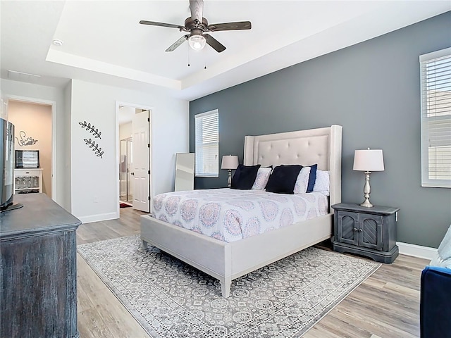 bedroom featuring a tray ceiling, light wood-style flooring, and multiple windows