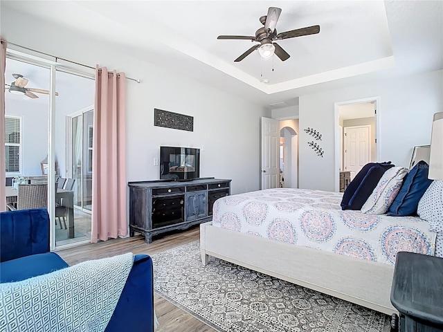 bedroom featuring arched walkways, light wood-type flooring, a raised ceiling, and access to outside