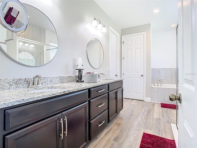 full bathroom with a sink, a garden tub, wood finished floors, and double vanity