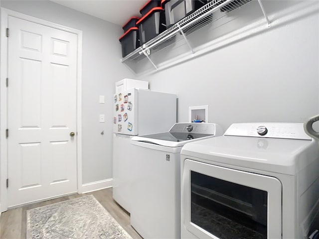 clothes washing area featuring washing machine and clothes dryer, laundry area, light wood finished floors, and baseboards