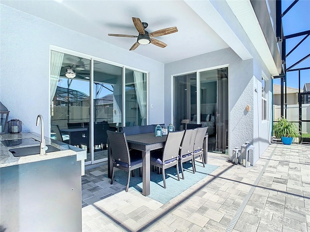 view of patio / terrace featuring outdoor dining space, glass enclosure, ceiling fan, and a sink