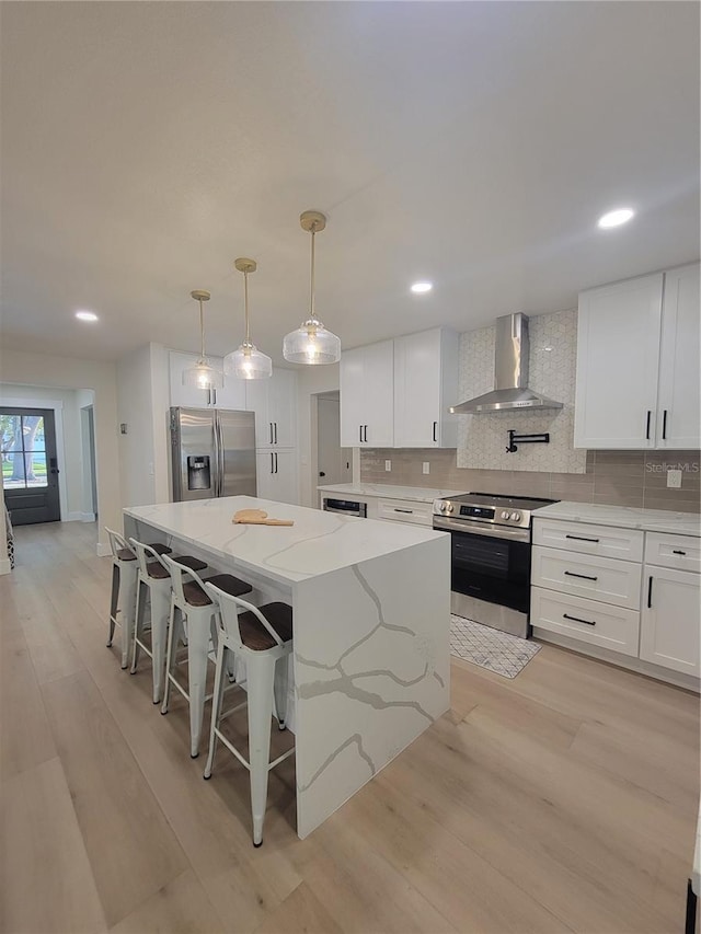 kitchen featuring tasteful backsplash, light wood finished floors, a center island, wall chimney range hood, and stainless steel appliances