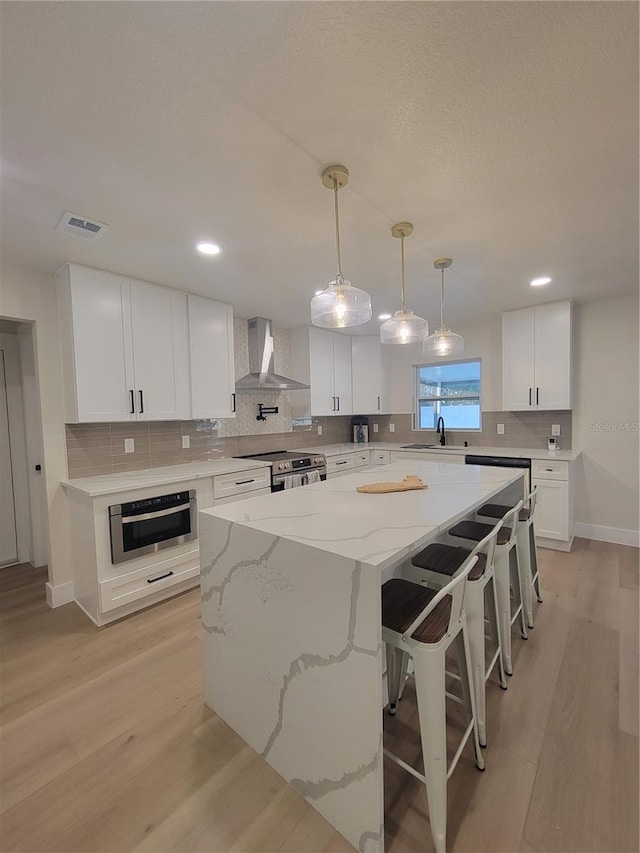 kitchen with a center island, white cabinetry, light wood-style floors, stainless steel electric range, and wall chimney range hood