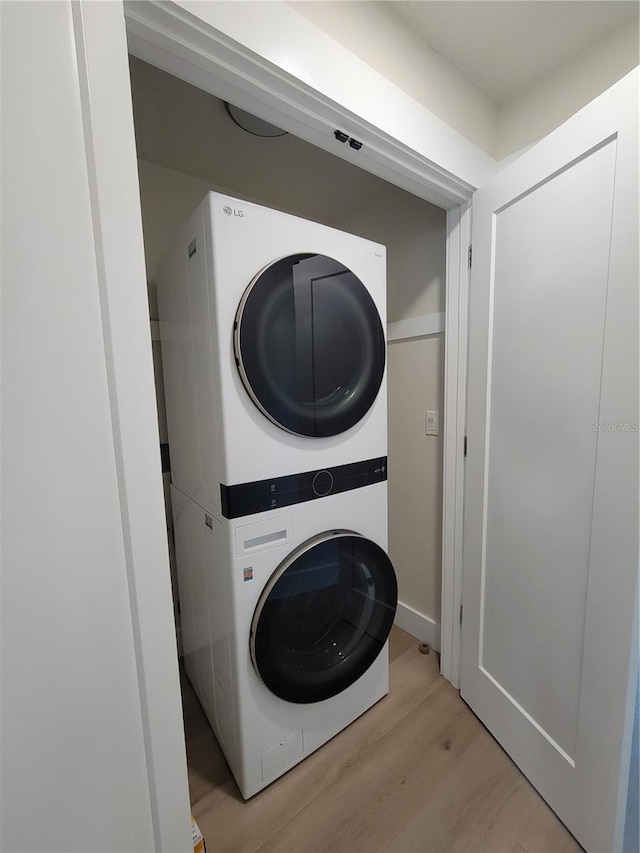 clothes washing area featuring laundry area, light wood-type flooring, and stacked washing maching and dryer