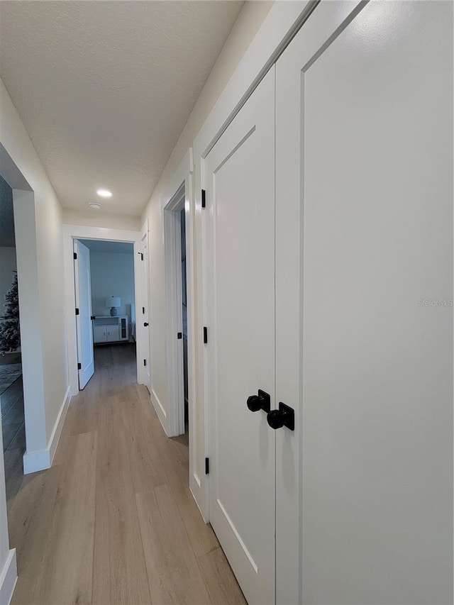 corridor with light wood finished floors, a textured ceiling, and baseboards