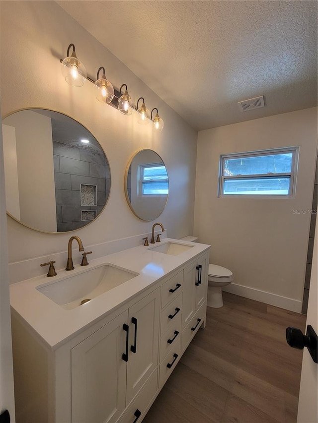 bathroom featuring visible vents, a textured ceiling, wood finished floors, and a sink