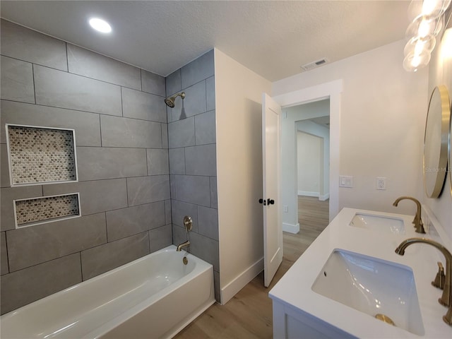 bathroom with wood finished floors, tub / shower combination, visible vents, and a sink