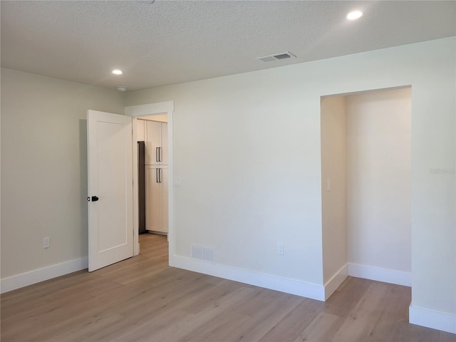 unfurnished room with visible vents, a textured ceiling, baseboards, and light wood-style floors