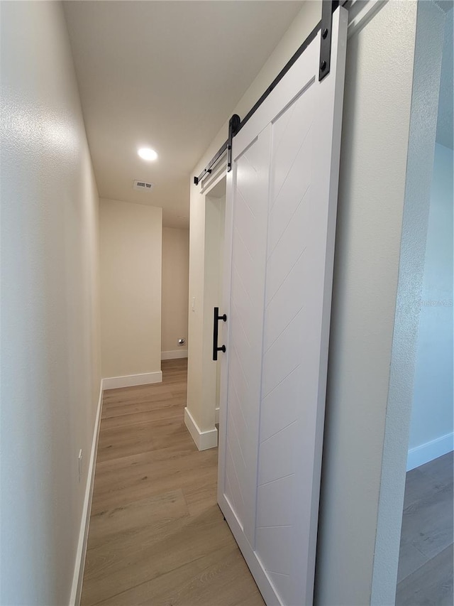 hallway featuring a barn door, light wood-style floors, baseboards, and visible vents