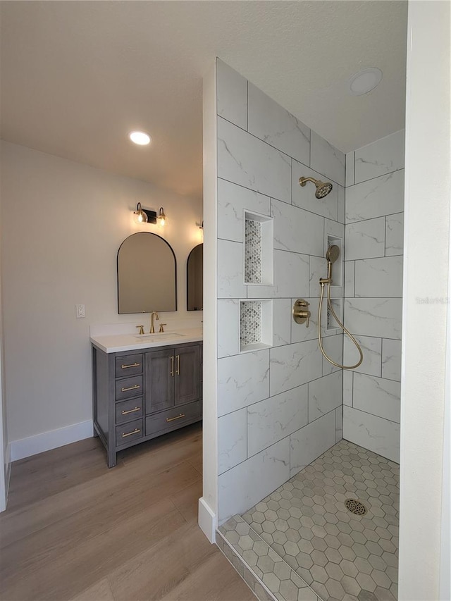 full bathroom featuring tiled shower, vanity, baseboards, and wood finished floors