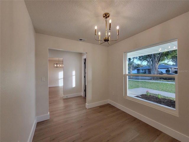 unfurnished dining area with a notable chandelier, baseboards, visible vents, and wood finished floors