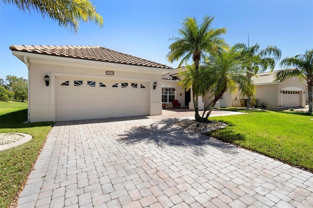 mediterranean / spanish-style house with a tiled roof, a front yard, stucco siding, decorative driveway, and an attached garage