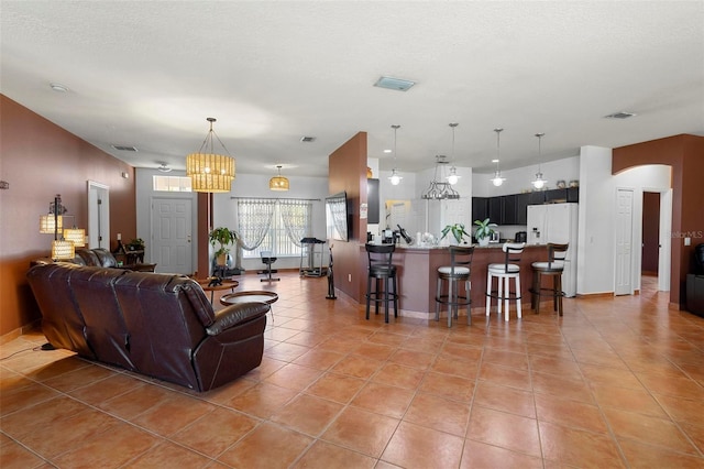 living area featuring light tile patterned floors, arched walkways, visible vents, and a textured ceiling