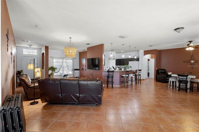 living area with visible vents, arched walkways, light tile patterned flooring, and ceiling fan with notable chandelier