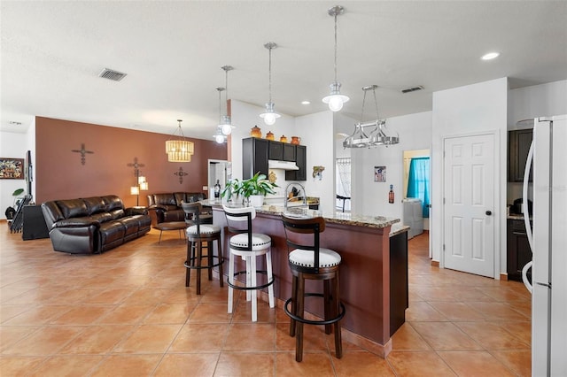 kitchen with visible vents, a breakfast bar, light stone counters, freestanding refrigerator, and light tile patterned flooring