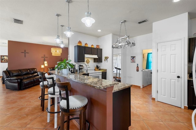 kitchen with light stone counters, electric stove, visible vents, and under cabinet range hood