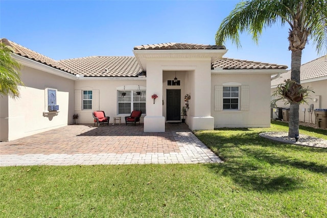 rear view of house with a patio, a tiled roof, a lawn, and stucco siding