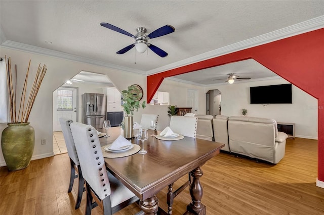 dining space with arched walkways, a textured ceiling, light wood-style flooring, and a ceiling fan