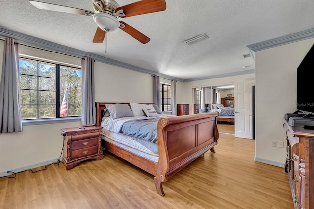 bedroom with a textured ceiling, light wood-style flooring, visible vents, and ornamental molding