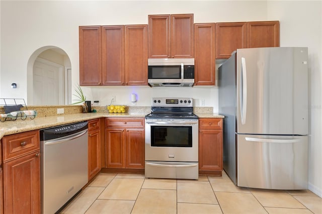 kitchen featuring light tile patterned floors, stainless steel appliances, light stone countertops, and brown cabinetry