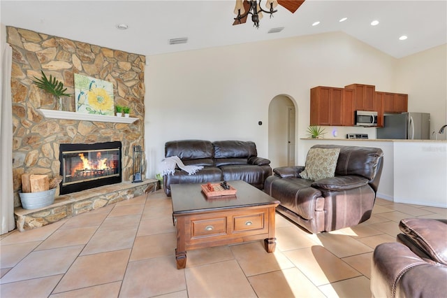 living room with visible vents, arched walkways, a fireplace, light tile patterned floors, and vaulted ceiling