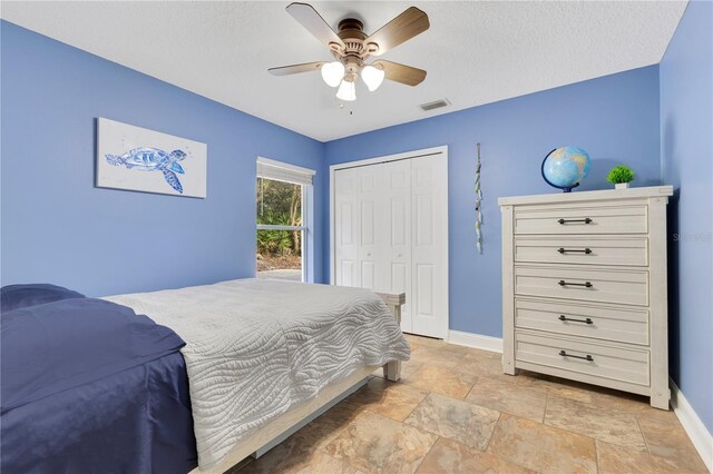 bedroom with visible vents, baseboards, a closet, stone finish floor, and a ceiling fan