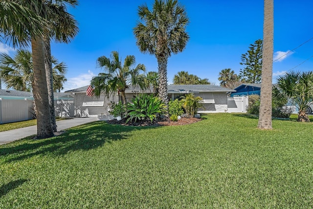 view of front of property with stucco siding, concrete driveway, a front lawn, and fence