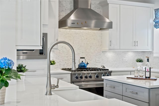 kitchen featuring white cabinetry, stainless steel stove, wall chimney exhaust hood, light countertops, and decorative backsplash