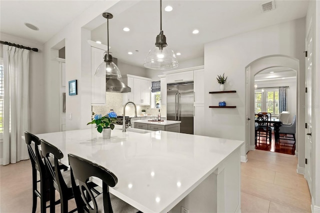 kitchen with visible vents, an island with sink, tasteful backsplash, built in fridge, and arched walkways