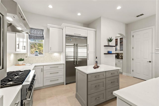 kitchen with visible vents, high quality appliances, white cabinetry, ventilation hood, and arched walkways