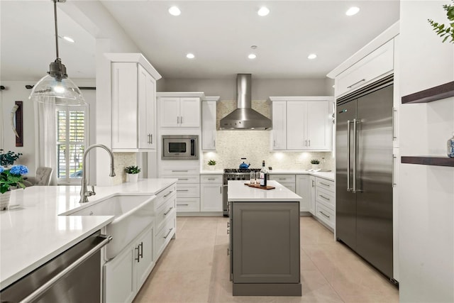 kitchen with a sink, light countertops, built in appliances, white cabinetry, and wall chimney exhaust hood