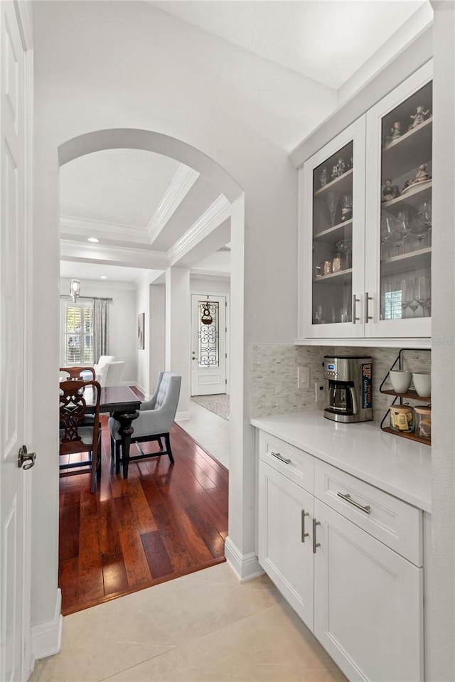 bar with a tray ceiling, light wood-style flooring, arched walkways, ornamental molding, and backsplash