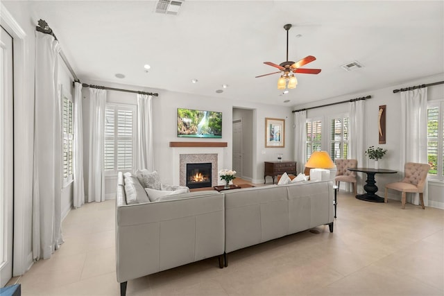 living room featuring a glass covered fireplace, a ceiling fan, and visible vents