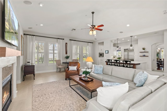 living area featuring light tile patterned floors, visible vents, recessed lighting, arched walkways, and a high end fireplace