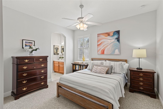 bedroom with light carpet, a ceiling fan, connected bathroom, arched walkways, and baseboards