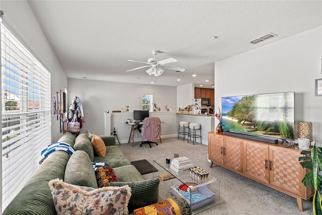 living room with visible vents, a ceiling fan, a textured ceiling, baseboards, and light colored carpet