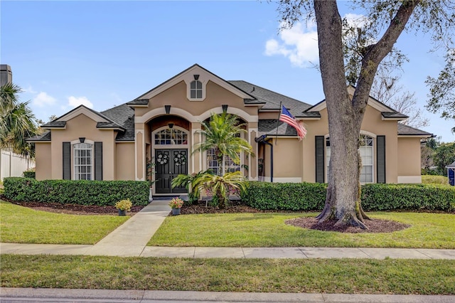 view of front of home with stucco siding, a front lawn, and a shingled roof