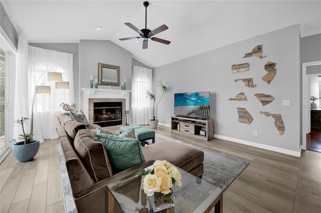 living room with baseboards, ceiling fan, lofted ceiling, a fireplace, and light wood-style floors