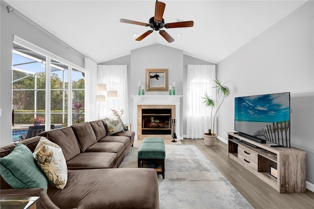 living room featuring baseboards, ceiling fan, vaulted ceiling, a fireplace, and wood finished floors